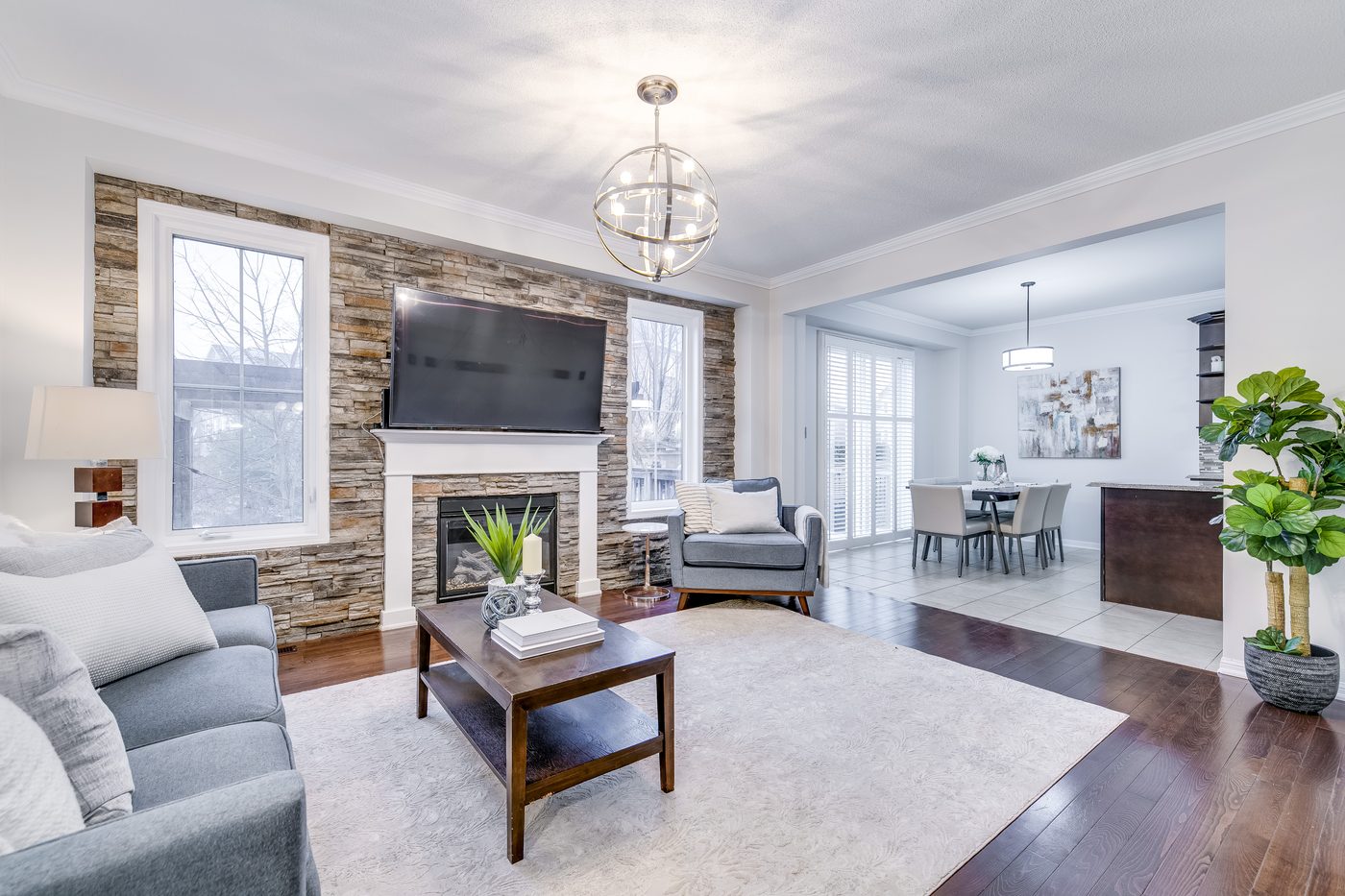A living room with a stone fireplace, open to the dining room